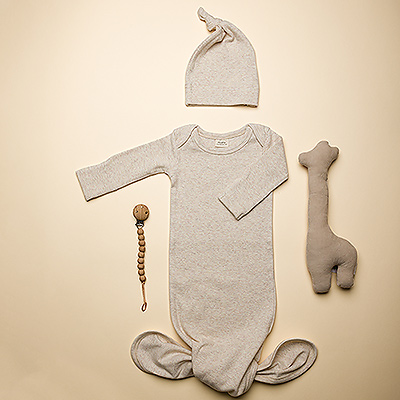 Welcome the new baby with this Mushie baby essentials gift set! This newborn gift includes an organic cotton knotted baby gown with matching beanie, food-grade silicone pacifier holder, and charming organic cotton giraffe rattle by Trixie.