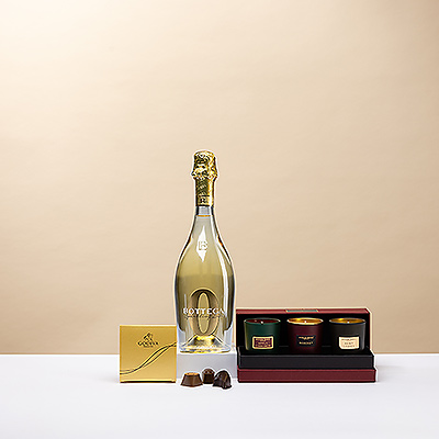 Profitez d'une soirée de Noël confortable à la maison avec de luxueuses bougies parfumées, un mini ballotin Godiva en or de quatre pièces et une boisson pétillante non alcoolisée Bottega Zero.